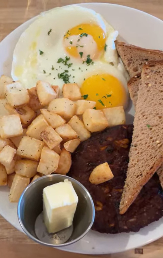 Plate with two sunny-side-up eggs, toast, home fries, a patty, and a small cup of butter&mdash;an energizing breakfast to start your day before heading out on your Churchill Northern Lights tour.