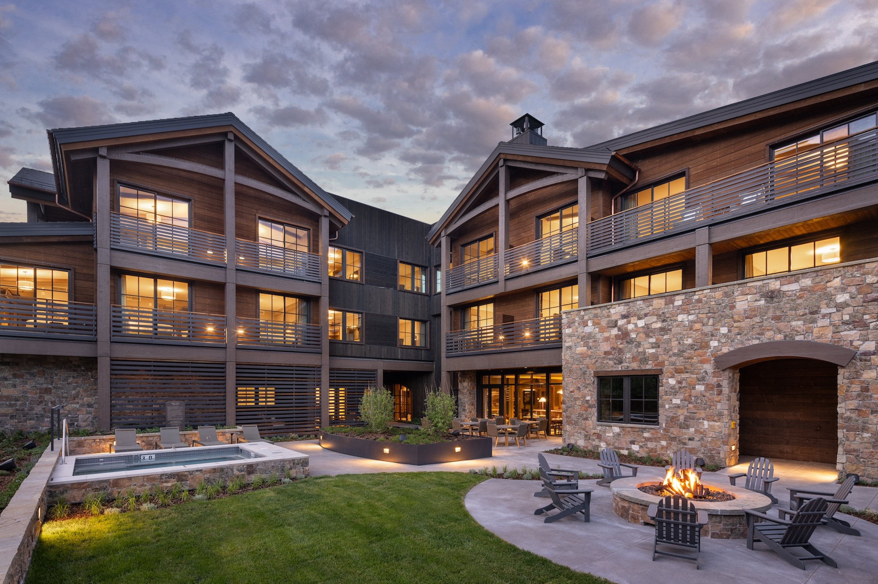 A modern lodge with balconies, large windows, a fire pit, and outdoor seating at sunset, reminiscent of the inviting ambiance found at Rusty Parrot Lodge and Spa.