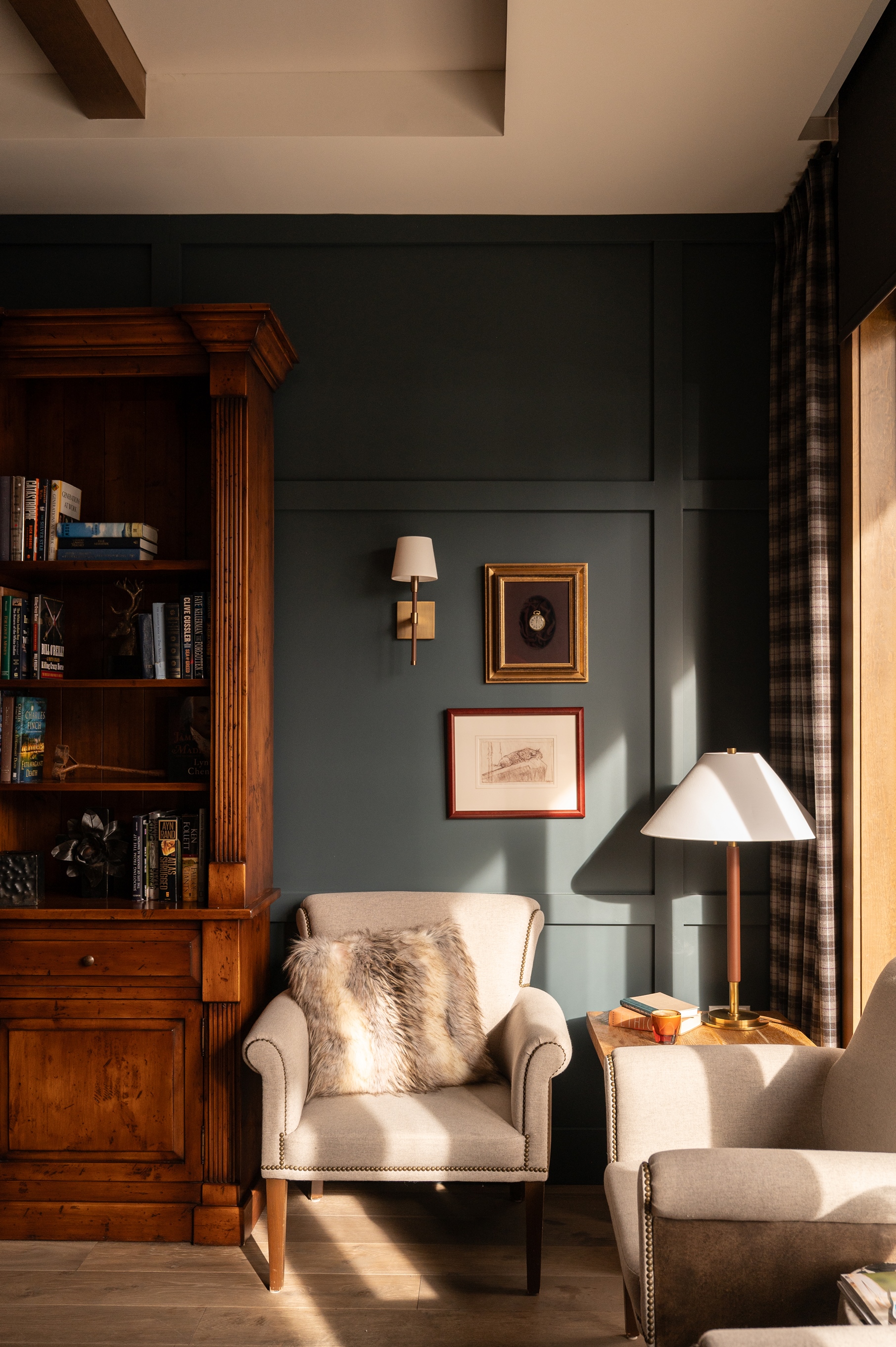 Cozy reading nook with armchairs, a lamp, a wooden bookshelf, and framed art on a dark-paneled wall, reminiscent of the inviting ambiance found at the Rusty Parrot Lodge and Spa.