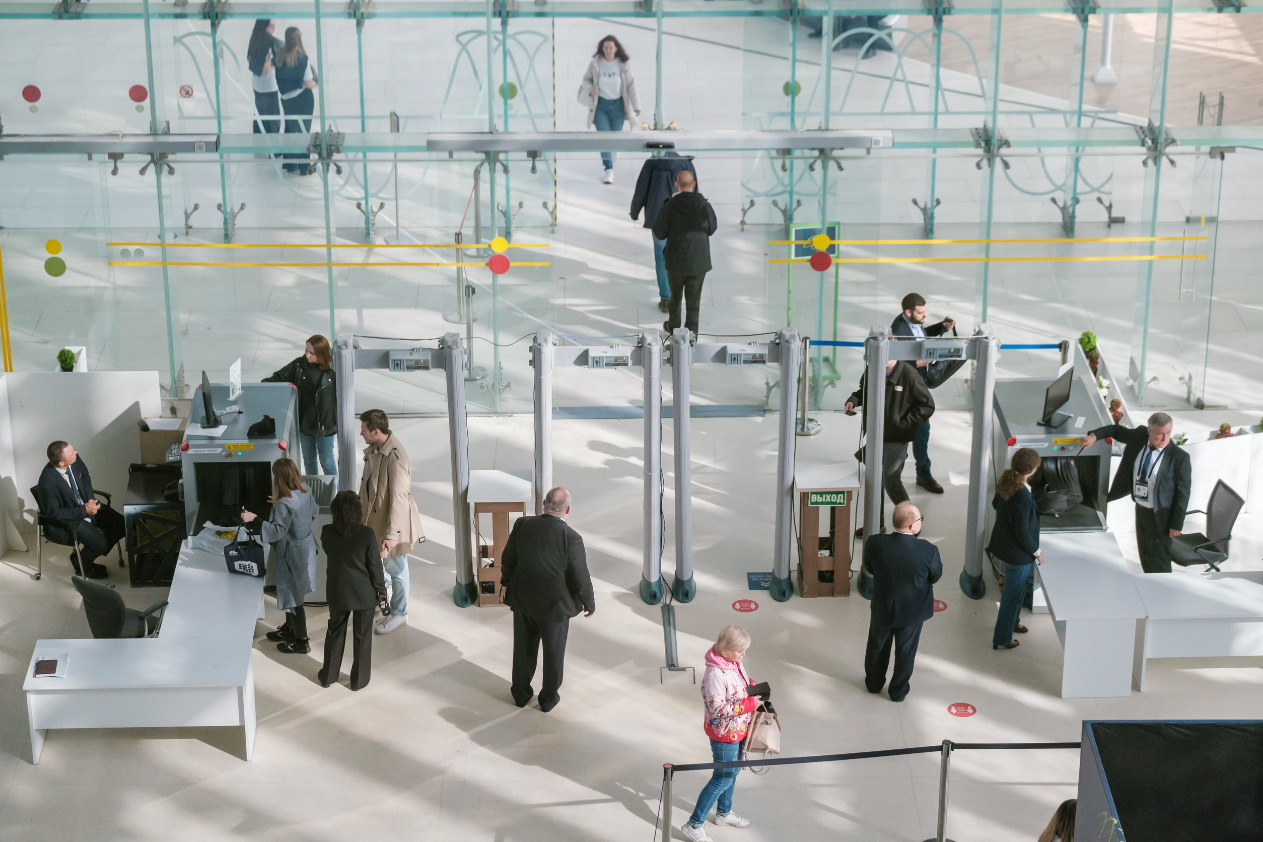 People pass through security gates in a modern, bright building with glass walls and several desks, enjoying convenient airport amenities along the way.
