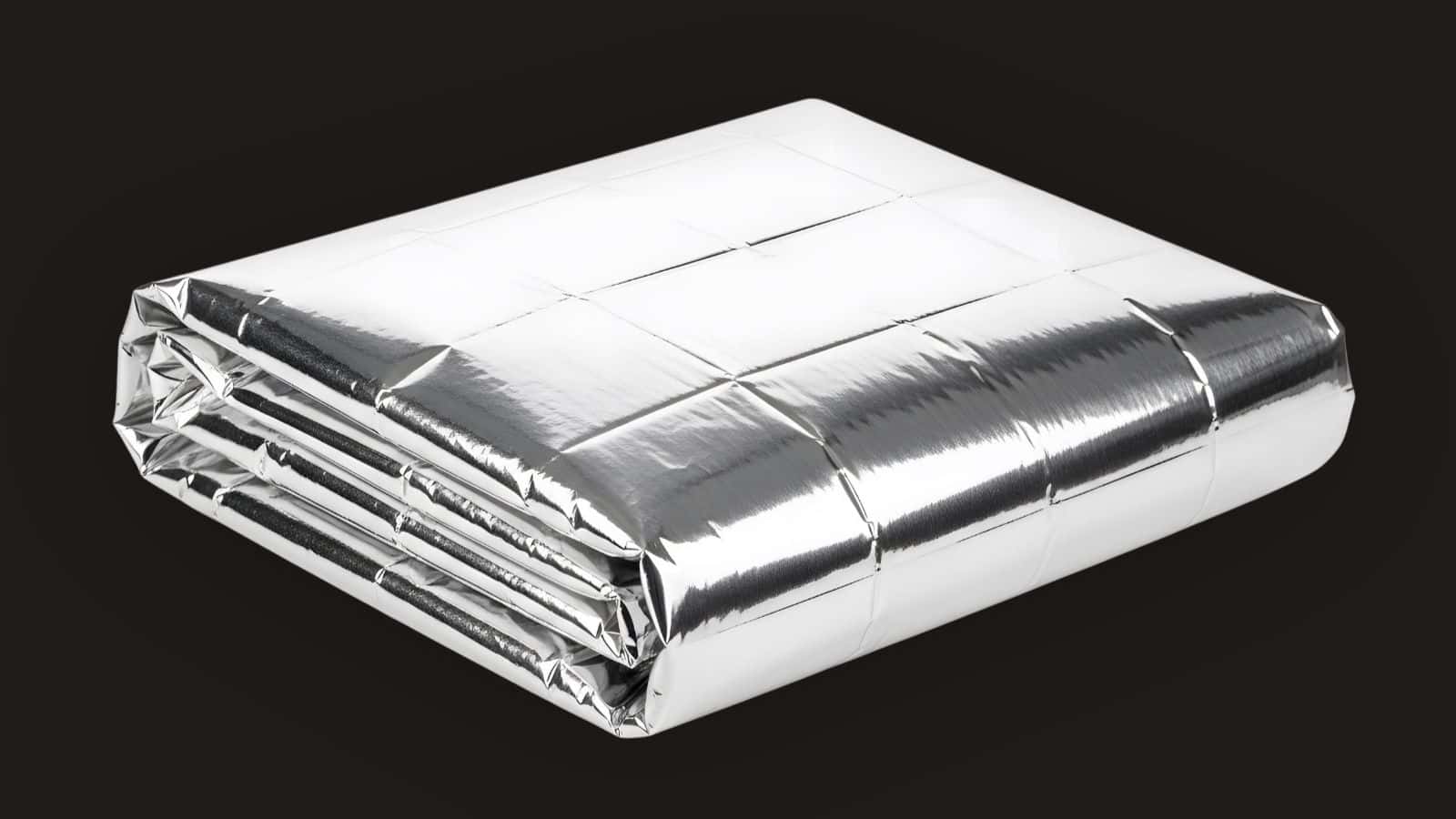 Folded silver emergency blanket with a reflective surface, set against a plain black background—a must-have among travel essentials for hiking or unpredictable weather.