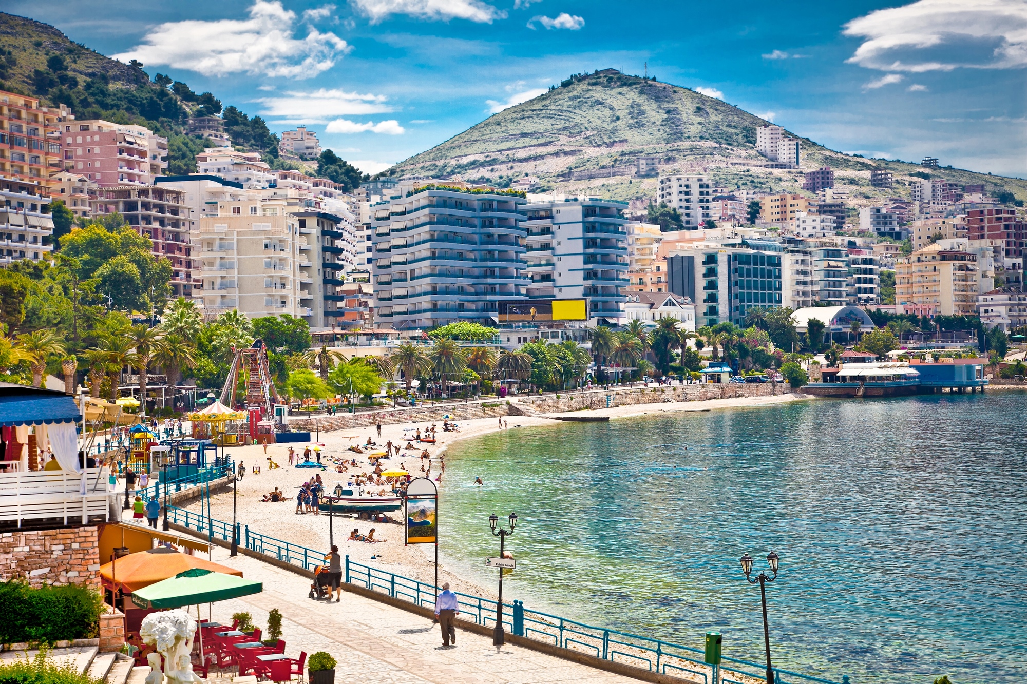A coastal city with a beach, people, palm trees, modern buildings, and a green hill in the background&mdash;this picturesque spot is one of the best-kept european destination dupes for travelers seeking beauty without the crowds.