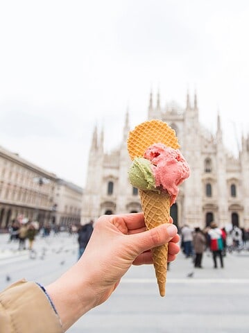 Hand holding gelato cone with wafers in front of a cathedral in a busy city square—a delicious moment from a food tour.