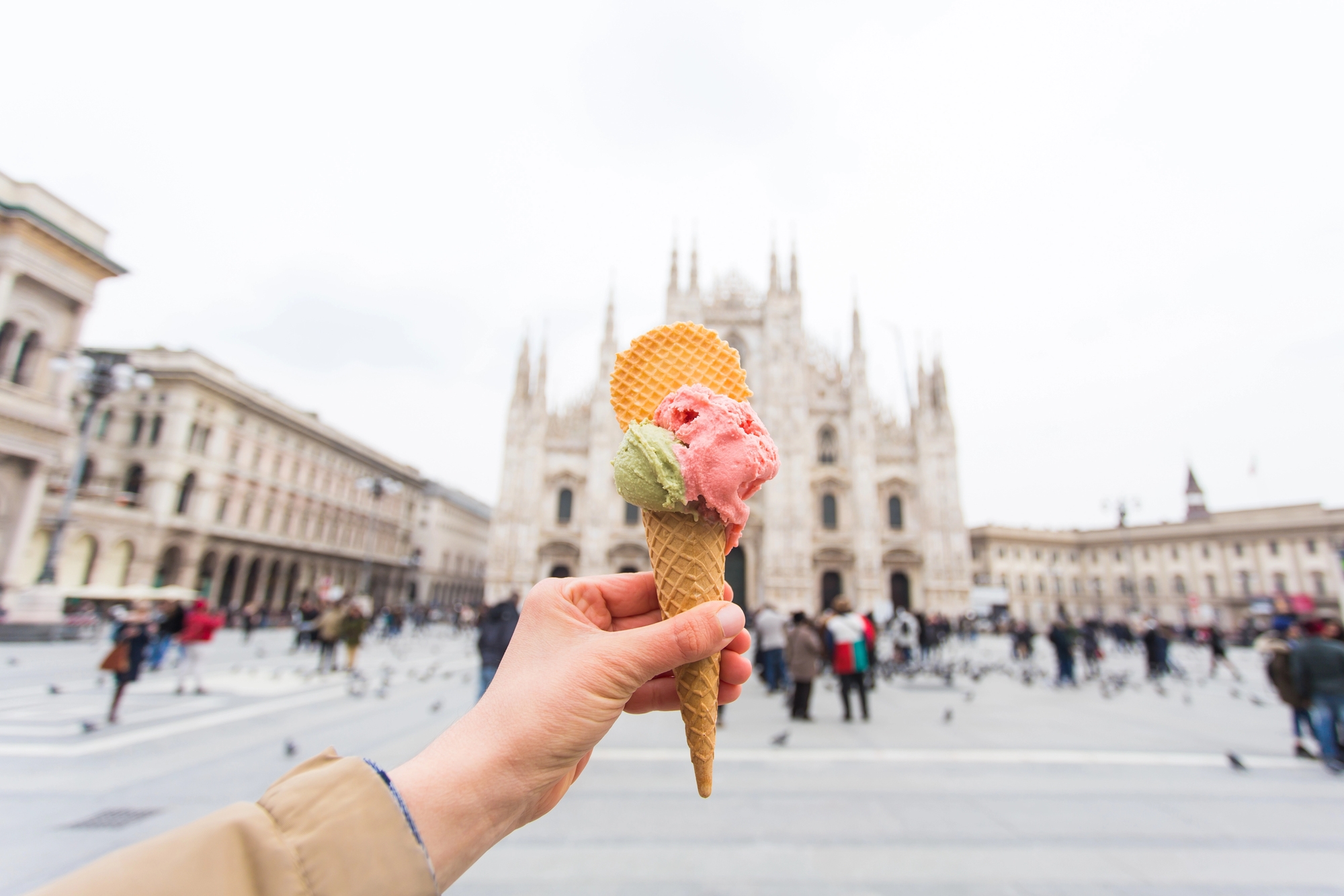 Hand holding gelato cone with wafers in front of a cathedral in a busy city square—a delicious moment from a food tour.