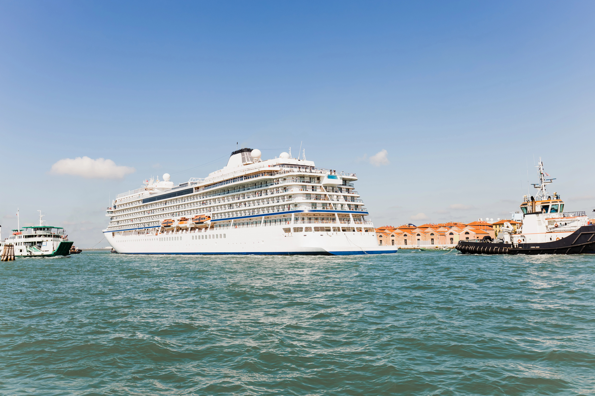 A white cruise ship sails near smaller boats on blue water under a clear sky, offering passengers an unforgettable Solar Eclipse Cruise experience.