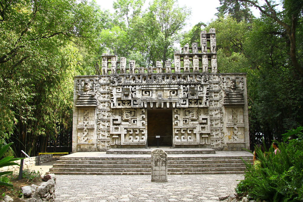 Ancient stone building with intricate carvings, surrounded by lush green trees and plants&mdash;an enchanting spot often considered one of the best European destination dupes for those seeking old-world charm without the crowds.