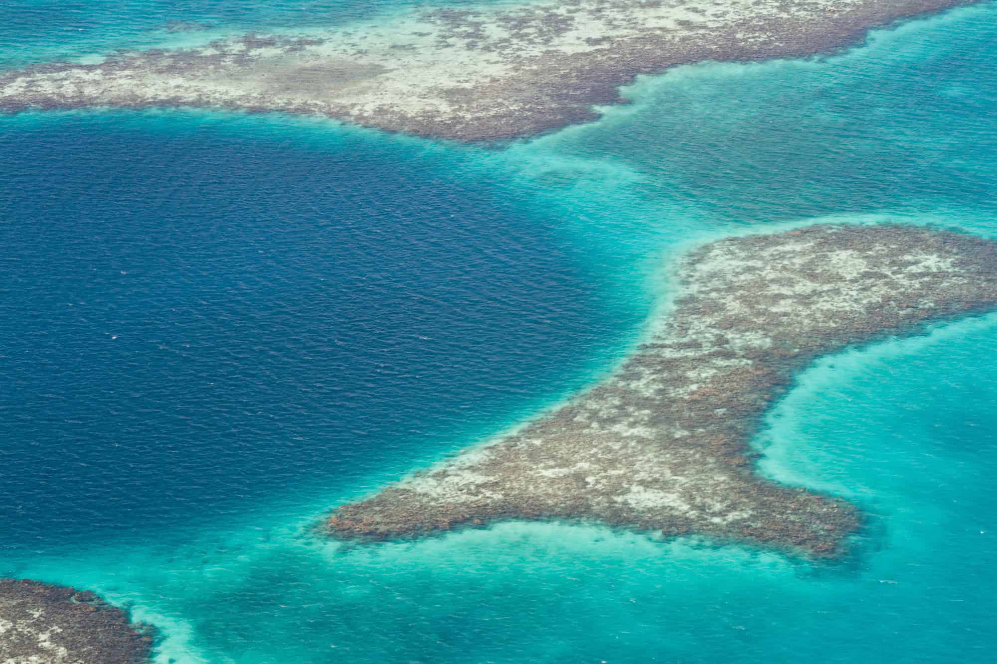 Aerial view of a deep blue ocean hole surrounded by coral reefs and turquoise water, capturing the breathtaking beauty you&rsquo;d experience on a Belize reef and ruins trip.