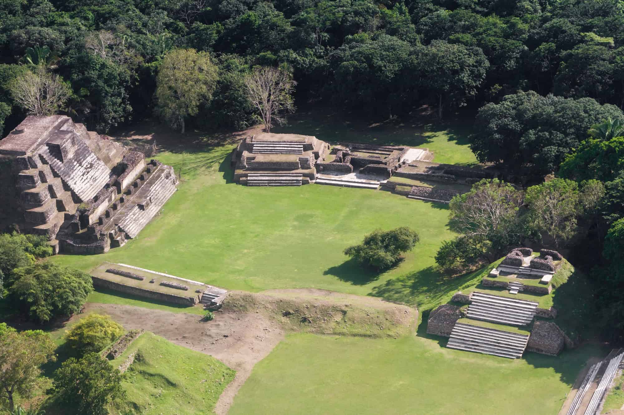 Aerial view of ancient stone ruins surrounded by trees and grassy areas, capturing the allure of a Belize reef and ruins trip.