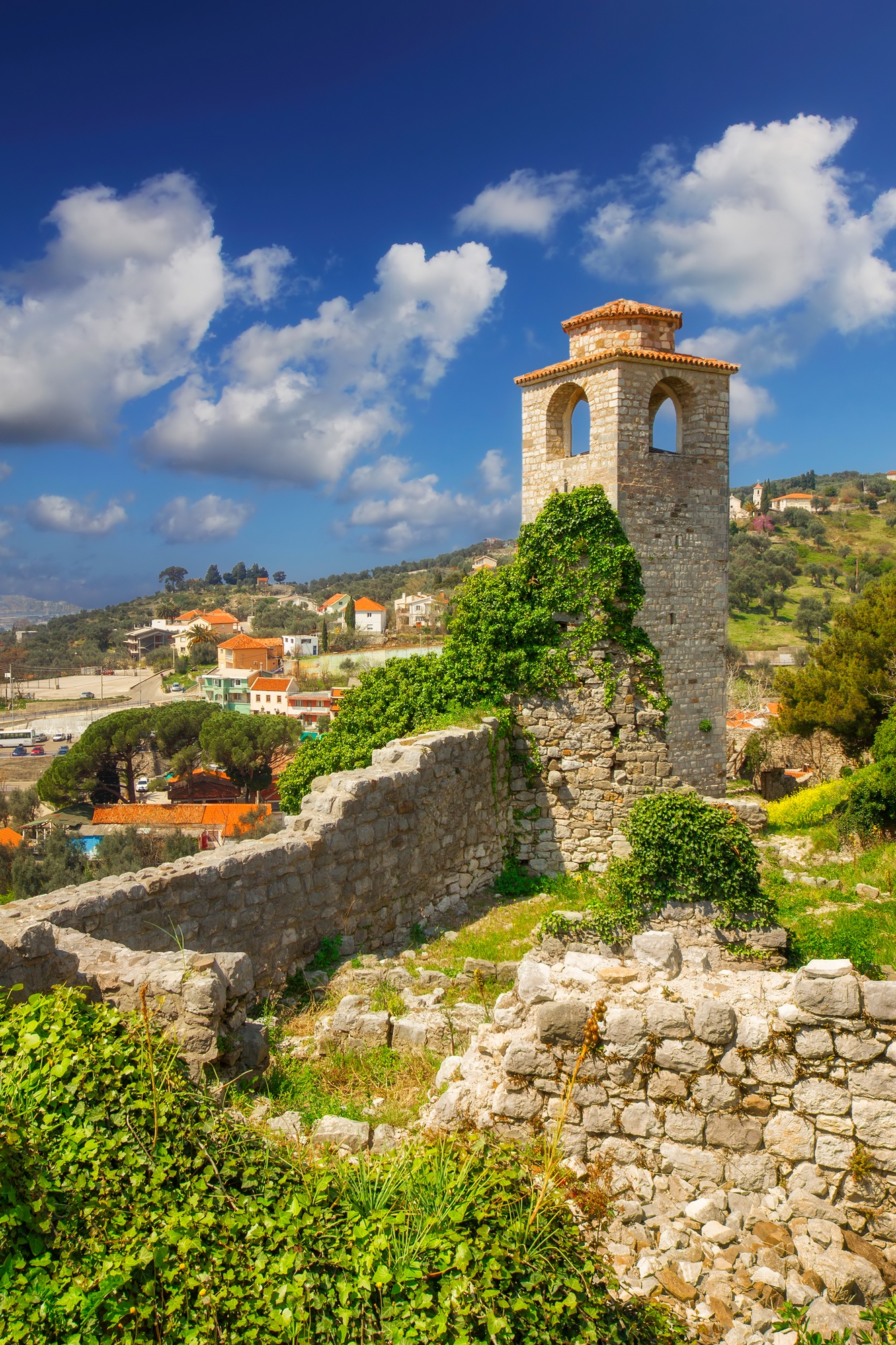 Stone tower covered in ivy, surrounded by ruins, with a village and blue sky in the background&mdash;a picturesque scene reminiscent of some of the best European destination dupes.