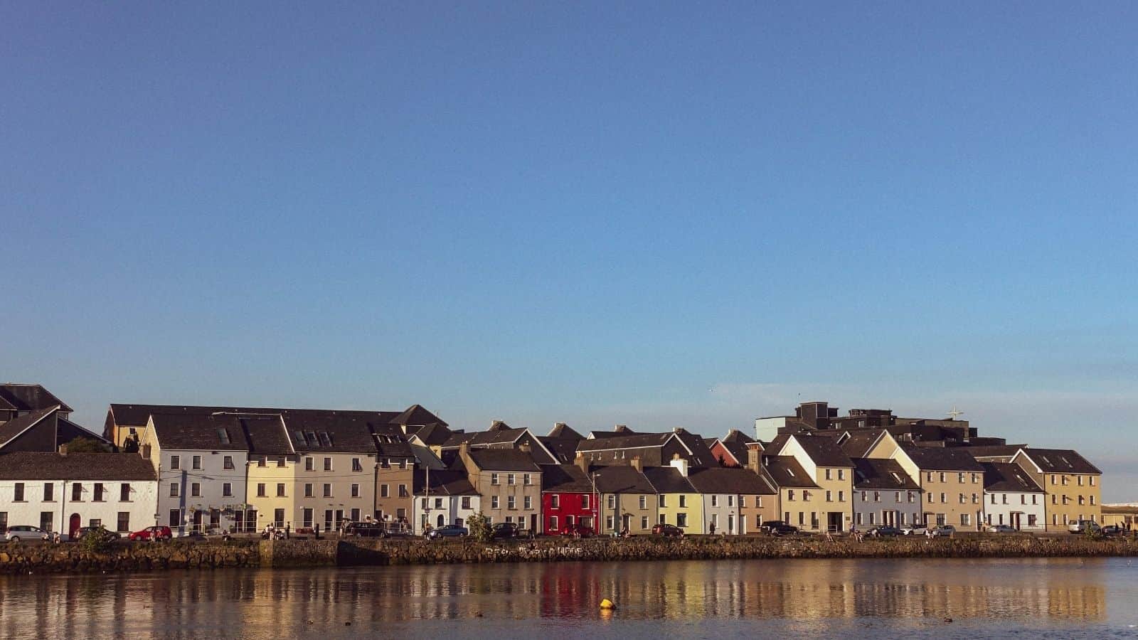 Row of colorful houses reflecting on calm water under a clear blue sky.