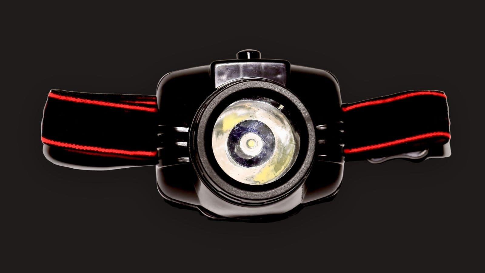 Black headlamp with a red-striped strap, viewed from the front against a plain black background—an ideal addition to your travel essentials, perfect for hiking adventures in unpredictable weather.