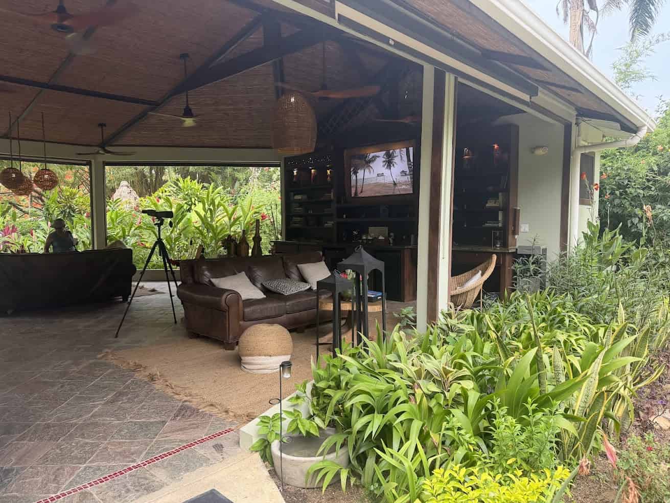 Open-air lounge with brown sofa, hammock, lush garden, and tropical plants visible through large windows—just like the serene settings described in The Rainforest Lodge at Sleeping Giant Review.