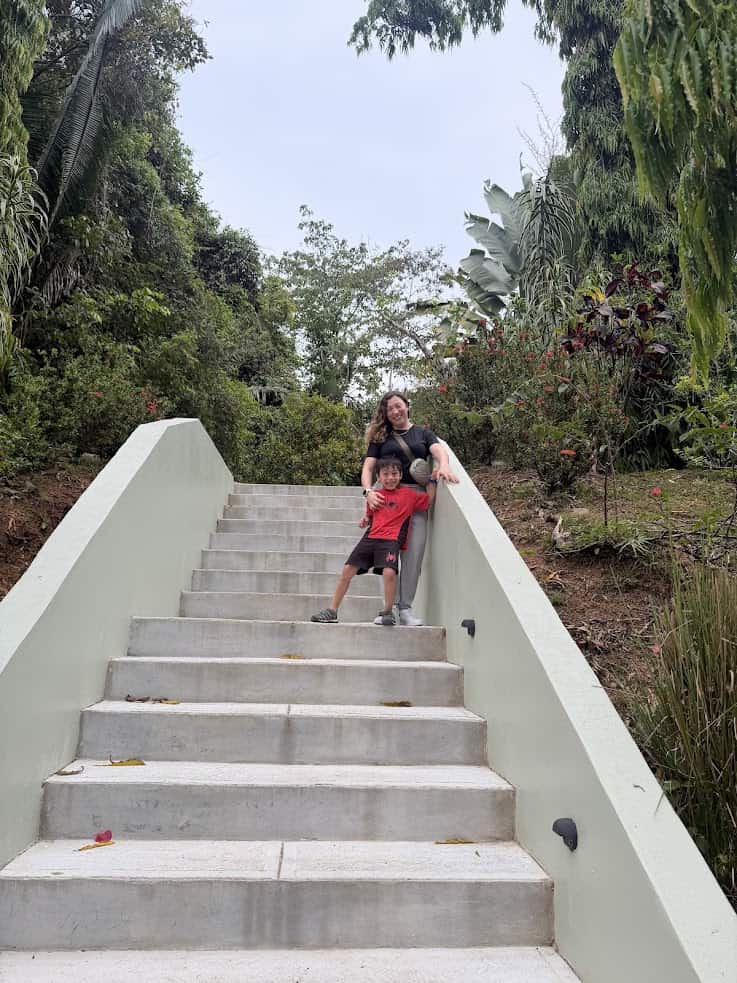 A woman and child smile, posing together on outdoor stairs surrounded by lush greenery and trees, capturing the tranquil ambiance described in The Rainforest Lodge at Sleeping Giant Review.