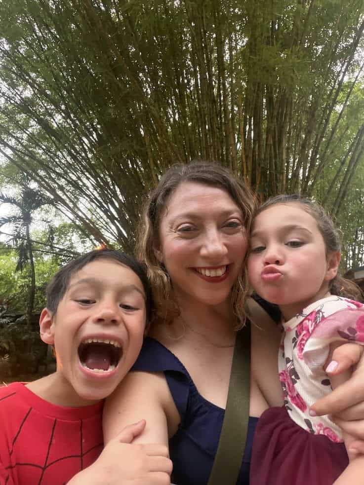 Woman smiling with two children outdoors at The Rainforest Lodge at Sleeping Giant—one making a silly face and the other with an open mouth—trees behind them, capturing a joyful moment surrounded by nature.