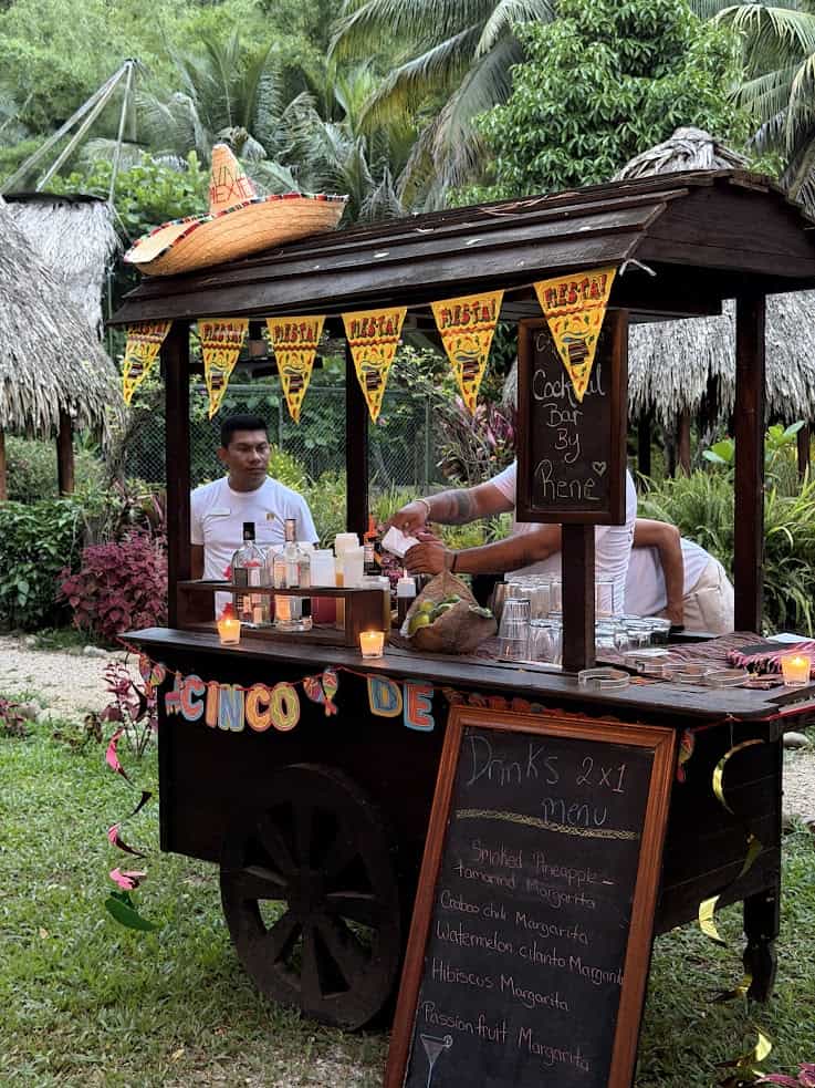 Cinco de Mayo celebrations come alive with an outdoor bar cart, decorated festively as two people prepare drinks beside a vibrant chalkboard menu—an experience reminiscent of the lively gatherings you might enjoy after reading The Rainforest Lodge at Sleeping Giant Review.