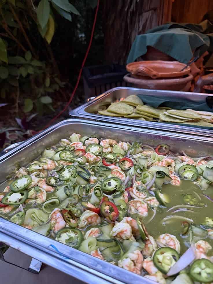Shrimp in green sauce with sliced jalapeños in a tray, with green tortilla chips in the background—a dish reminiscent of the vibrant flavors highlighted in The Rainforest Lodge at Sleeping Giant Review.
