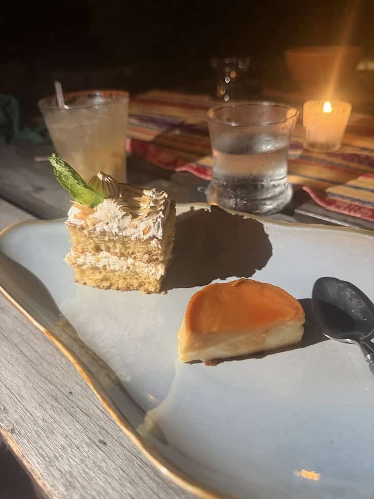 Two desserts on a plate—a beautifully decorated cake slice and a smooth custard—are served with drinks and a candle glowing softly in the background. This picture captures the delightful culinary presentation you can expect during your stay, as highlighted in The Rainforest Lodge at Sleeping Giant Review.