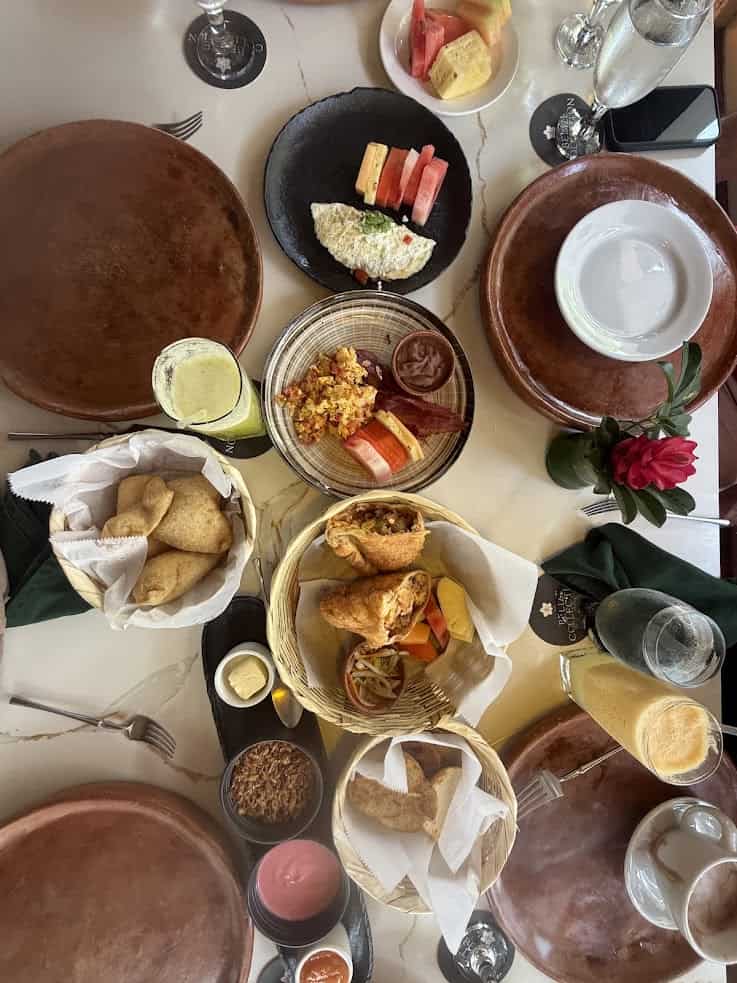 Table with assorted Latin American dishes, drinks, sauces, bread basket, and empty brown plates—an inviting spread reminiscent of a memorable evening at The Rainforest Lodge at Sleeping Giant.