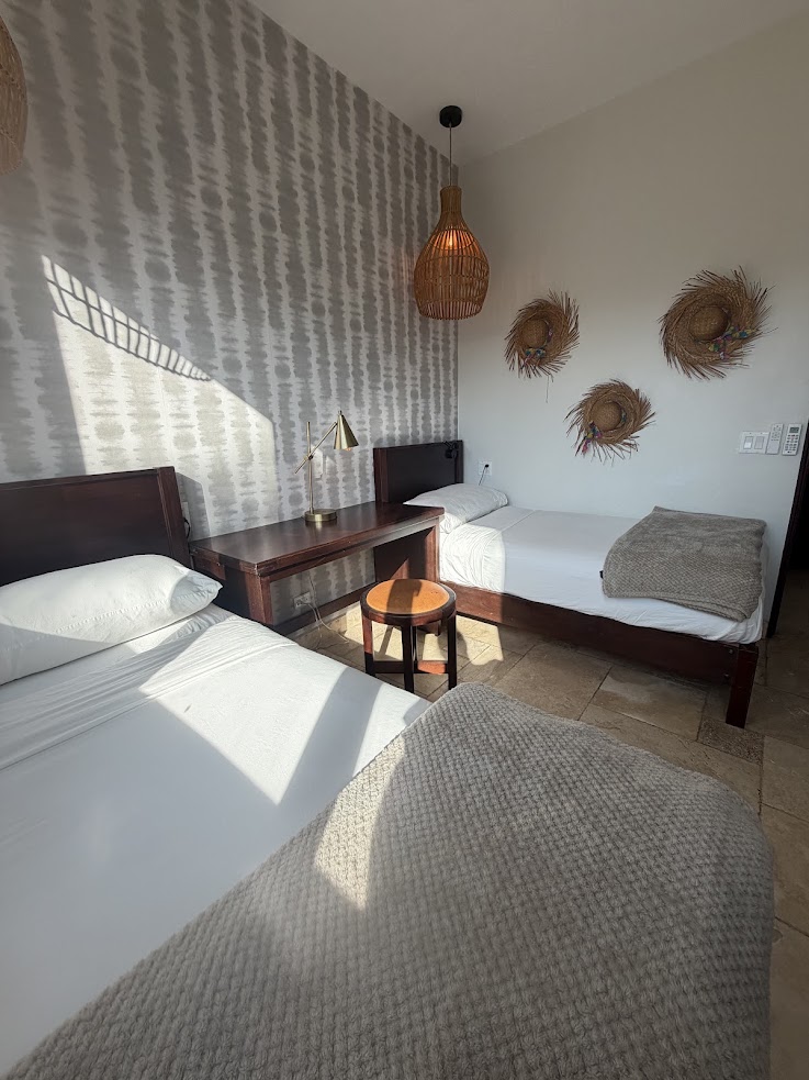 Two single beds, a desk, and woven wall decor in a bright, modern bedroom with patterned wallpaper create an inviting atmosphere reminiscent of the style praised in many The Lodge at Jaguar Reef reviews.