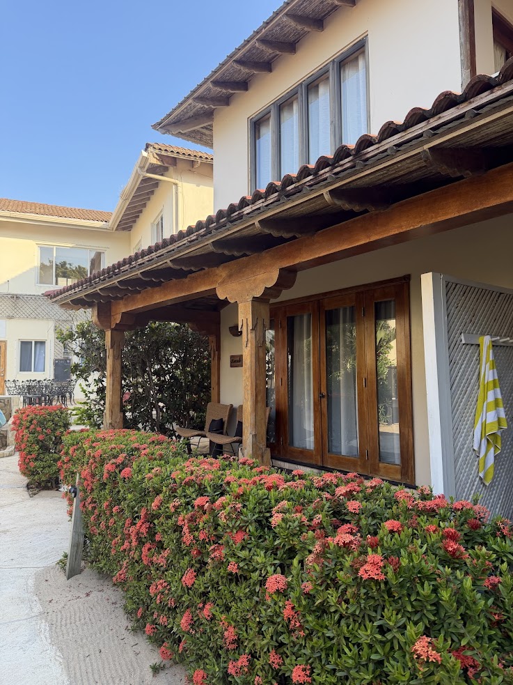 A house with a wooden porch, red flowers in front, and a yellow striped towel hanging outside evokes the laid-back charm often mentioned in the lodge at jaguar reef review.