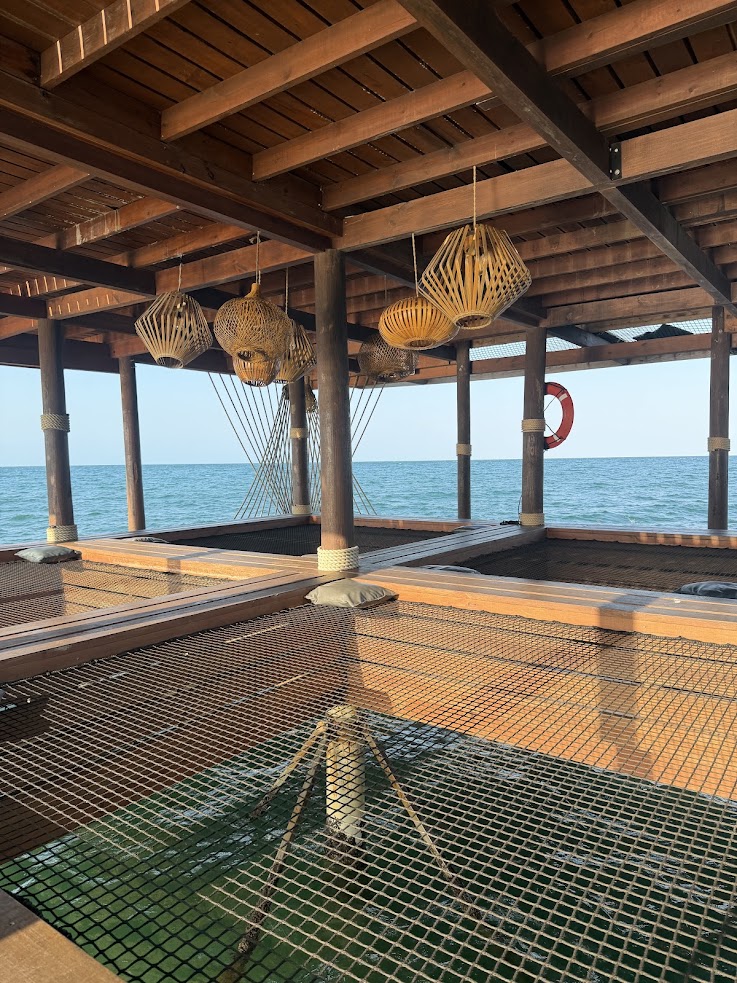 Wooden deck over the sea with nets, lanterns, and a distant lifebuoy under a sunny sky&mdash;reminiscent of scenes described in many a glowing The Lodge at Jaguar Reef review.