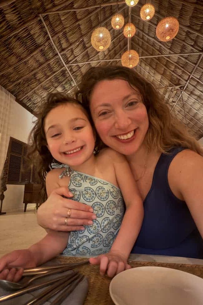 Smiling woman and child posing for a selfie at a warmly lit restaurant with a thatched roof, capturing the inviting atmosphere often mentioned in a The Lodge at Jaguar Reef review.