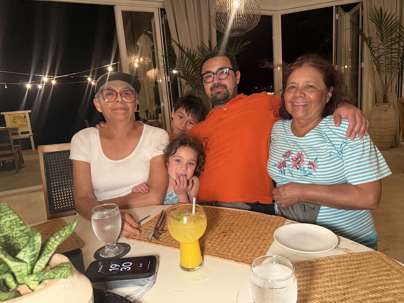 Five people sit at a dinner table with drinks, smiling at the camera in a warmly lit restaurant, capturing the inviting ambiance often mentioned in a glowing The Lodge at Jaguar Reef review.