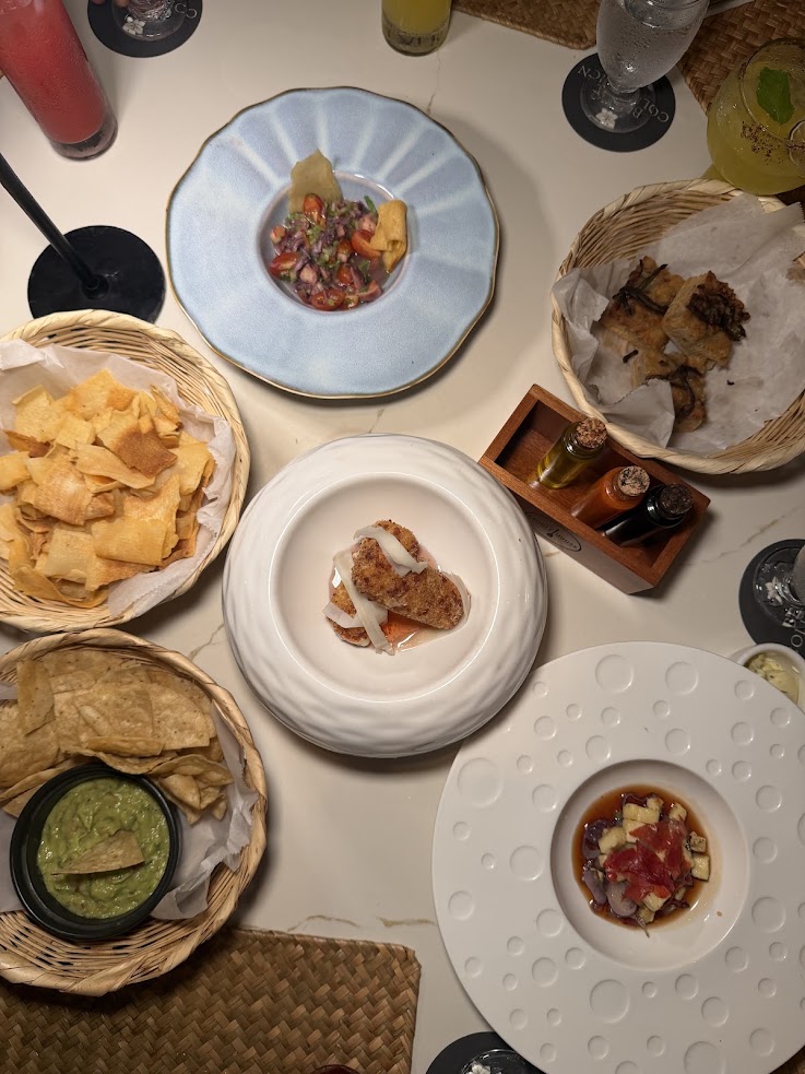 Tabletop with assorted appetizers: chips with guacamole, salsas, a small meat dish, and drinks in baskets and plates&mdash;an inviting spread reminiscent of the vibrant flavors described in many a glowing The Lodge at Jaguar Reef review.