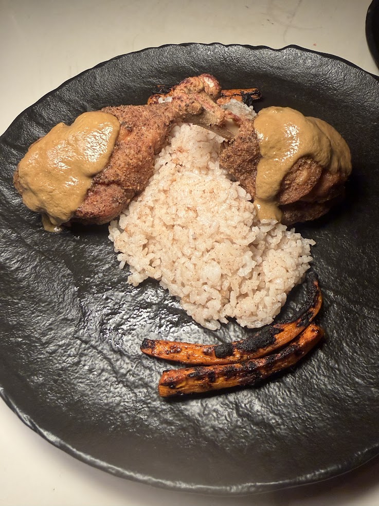 Two pieces of sauced chicken, rice, and grilled carrots are beautifully arranged on a black plate, reminiscent of the exquisite presentation mentioned in the lodge at jaguar reef review.