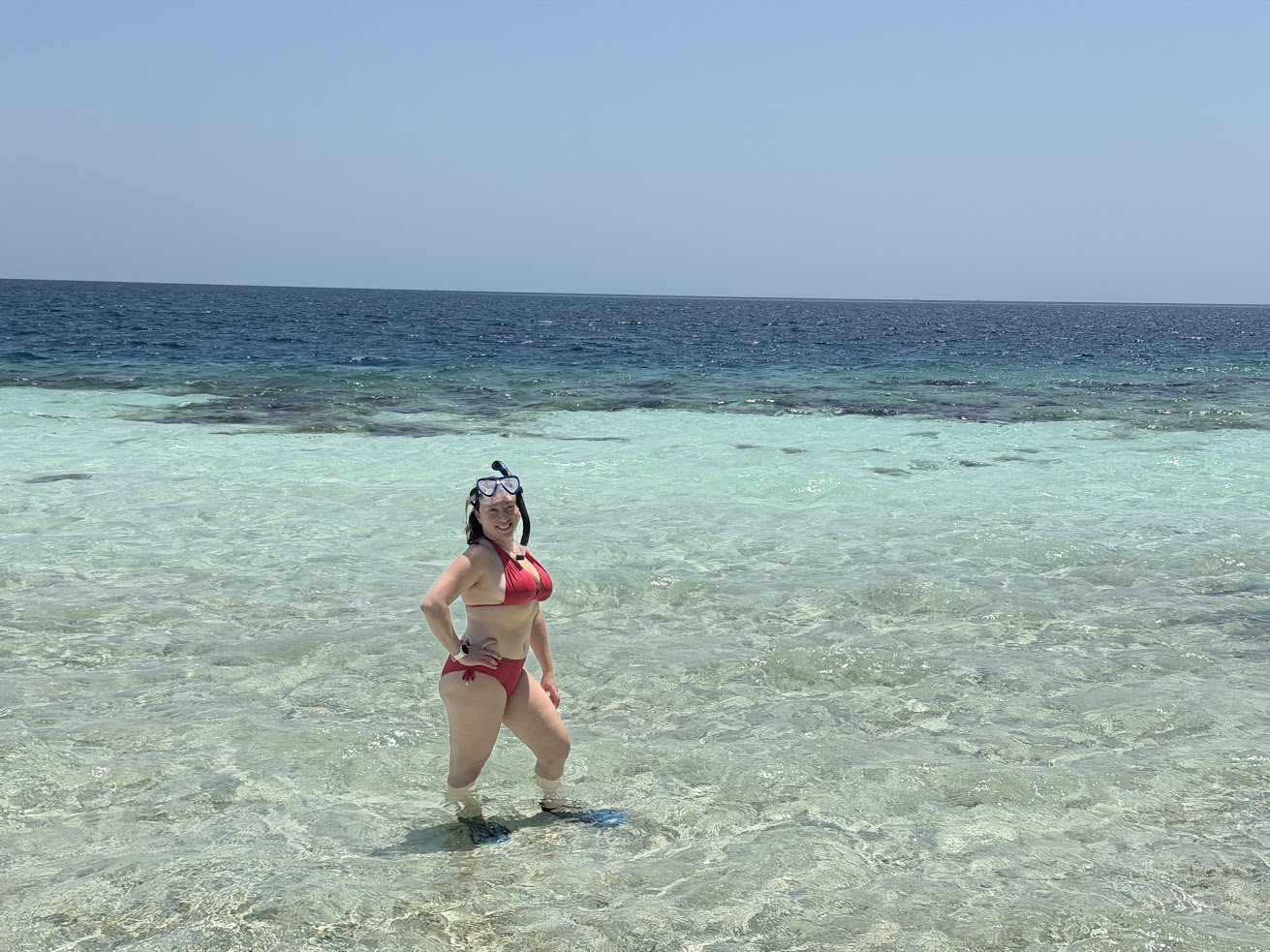 A woman in snorkel gear stands in clear, shallow ocean water under a bright sunny sky&mdash;a scene reminiscent of the beautiful settings often mentioned in a glowing The Lodge at Jaguar Reef review.