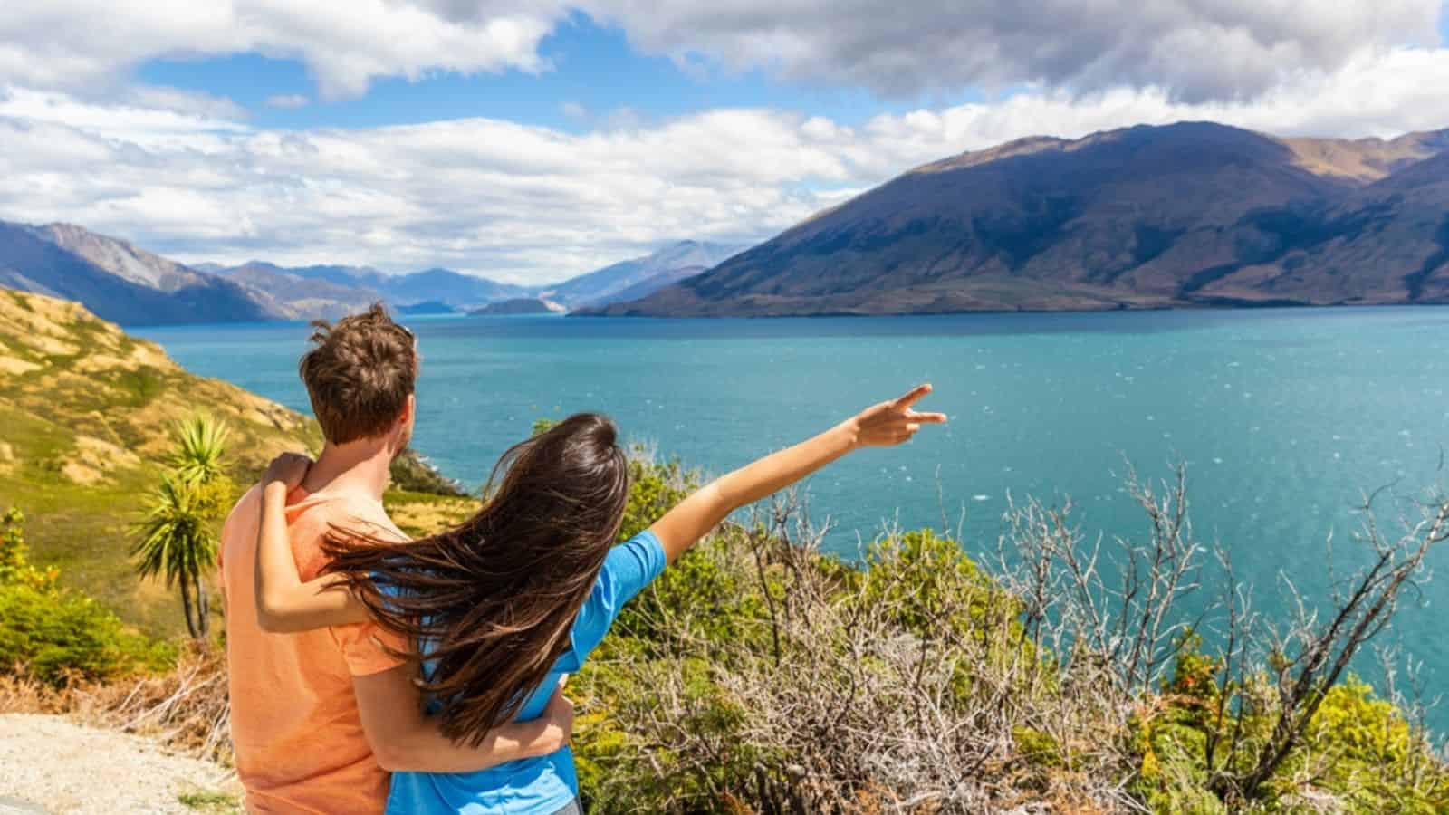 Two people embrace while looking at a blue lake and mountains under a partly cloudy sky, savoring the beauty found in some of the best countries for tourists.