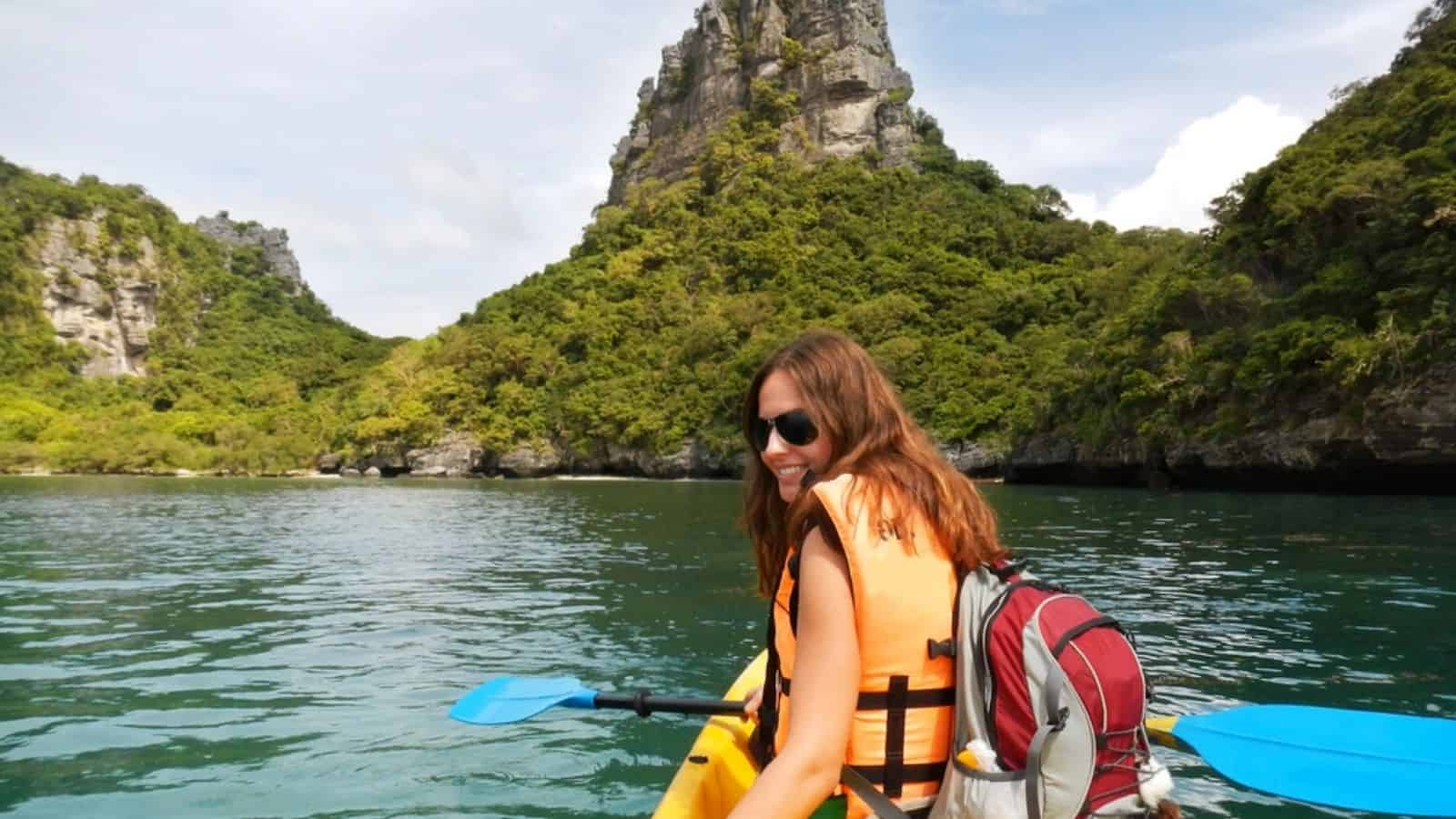 Woman in a life jacket kayaking on clear water with lush green mountains in the background, embodying travel safety while exploring one of the top countries for tourists.