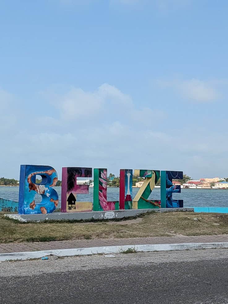 Large colorful &ldquo;BELIZE&rdquo; letters by the water, with buildings and a cloudy sky in the background&mdash;an inviting spot that captures the spirit of a belize reef and ruins trip.