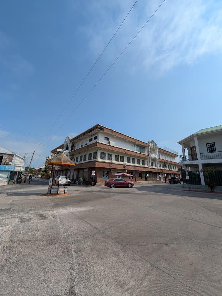 A three-story building with shops and cars at a street intersection under a clear blue sky, reminiscent of the vibrant sights you might encounter on a Belize reef and ruins trip.