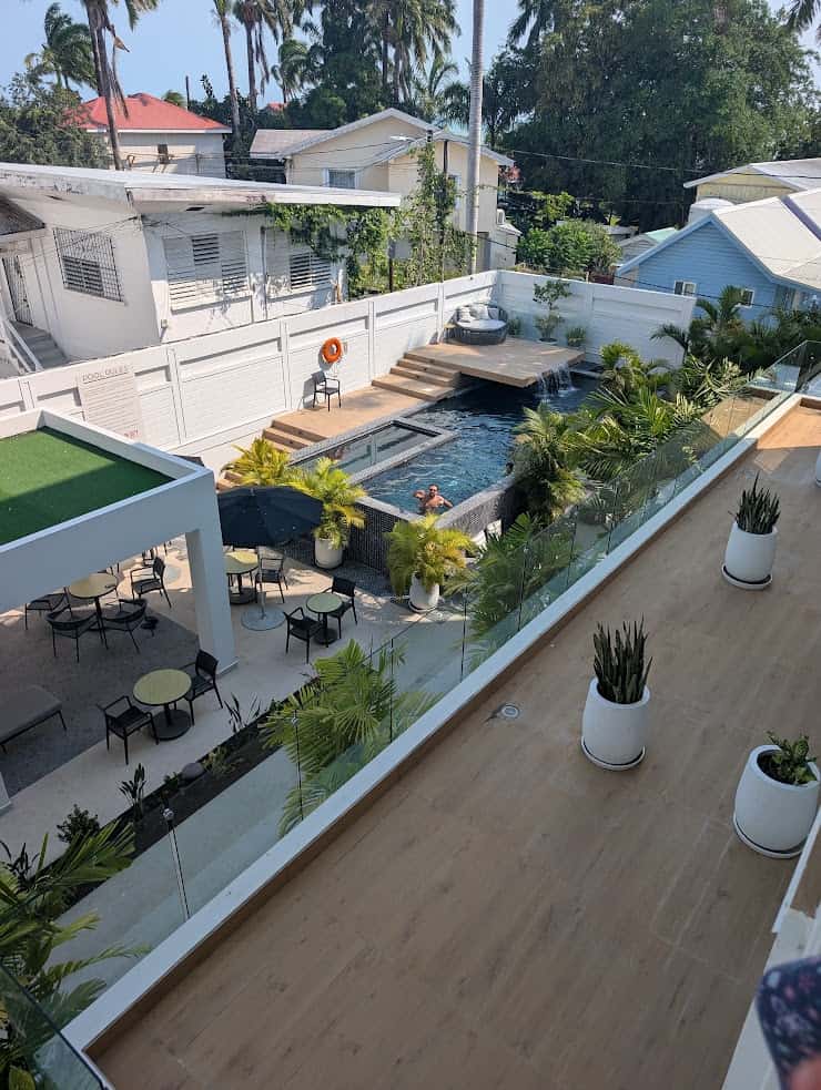 View from balcony of a pool area with tables, chairs, greenery, and white buildings in the background&mdash;perfect for relaxing after a day exploring the wonders of your Belize reef and ruins trip.
