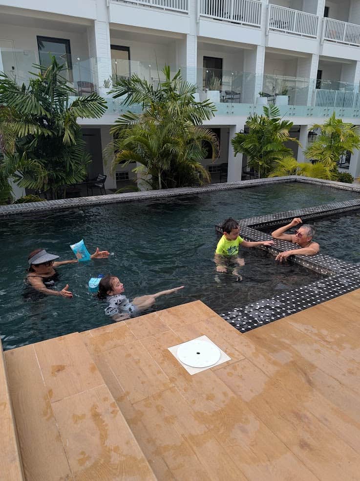 Four people swim and play in a pool near a hotel, surrounded by tropical plants and a wooden deck&mdash;the perfect place to unwind after a day exploring the wonders of a Belize reef and ruins trip.