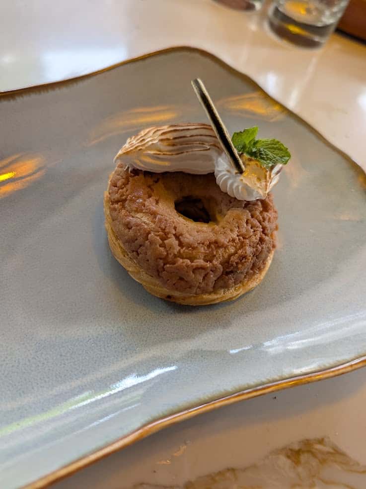 Small round pastry with cream, mint, and chocolate garnish, served on a light blue plate—just one of the delightful desserts you might enjoy after a meal at The Rainforest Lodge at Sleeping Giant. Review highlights often praise both presentation and flavor.