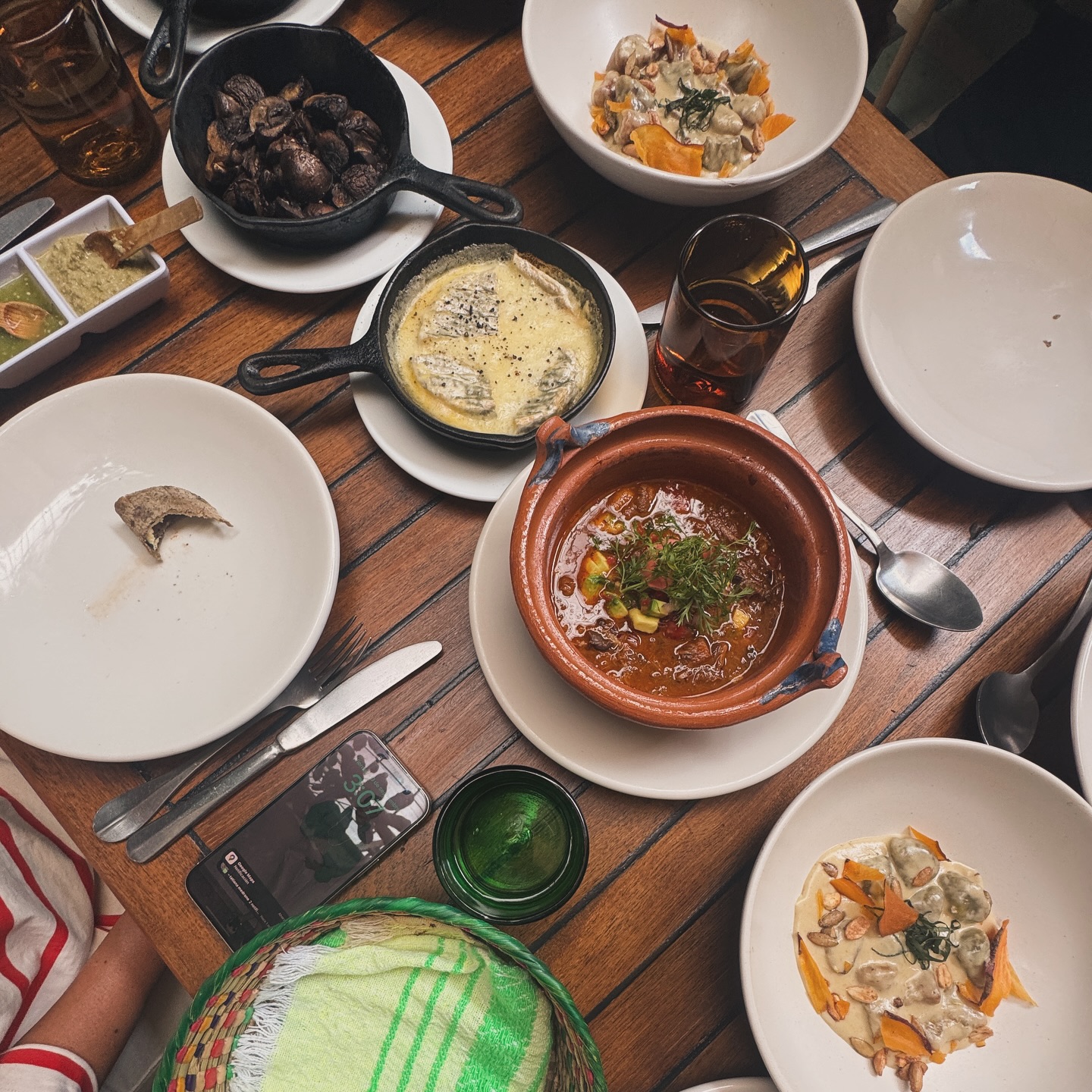 Wooden table with various dishes, drinks, utensils, and a phone, viewed from above during a food tour meal.