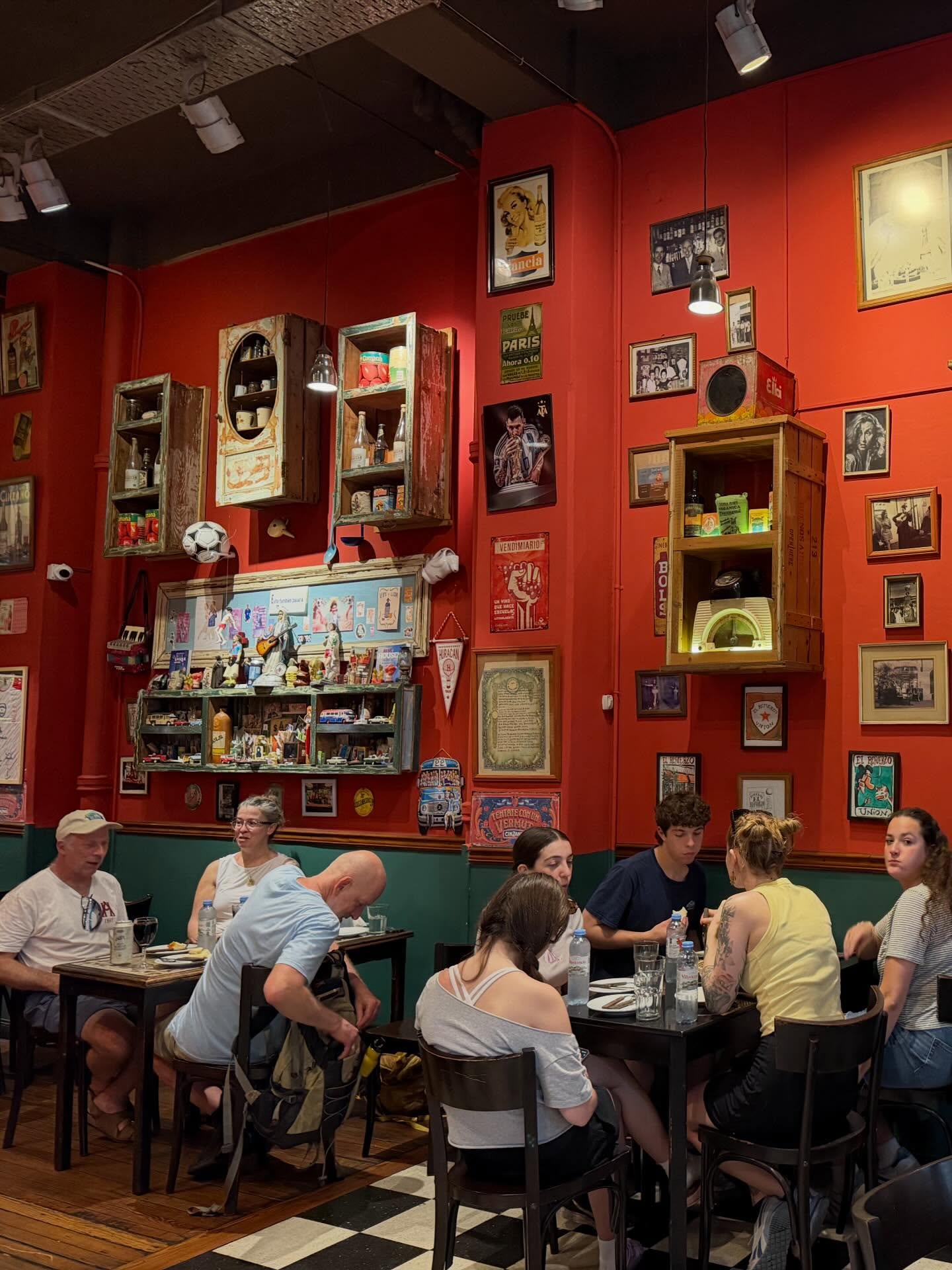 People dining in a cozy restaurant with eclectic red walls covered in vintage photos, shelves, and memorabilia—perfect for those seeking an authentic stop on their food tour.