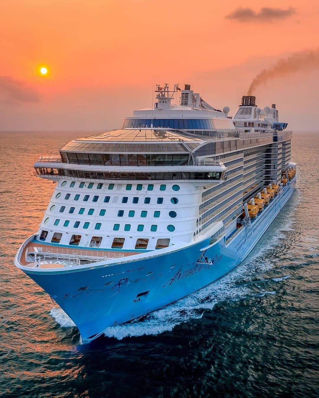 A large cruise ship sails on the ocean at sunset, with the sky glowing orange and the sun low&mdash;an unforgettable scene for guests aboard the Solar Eclipse Cruise.