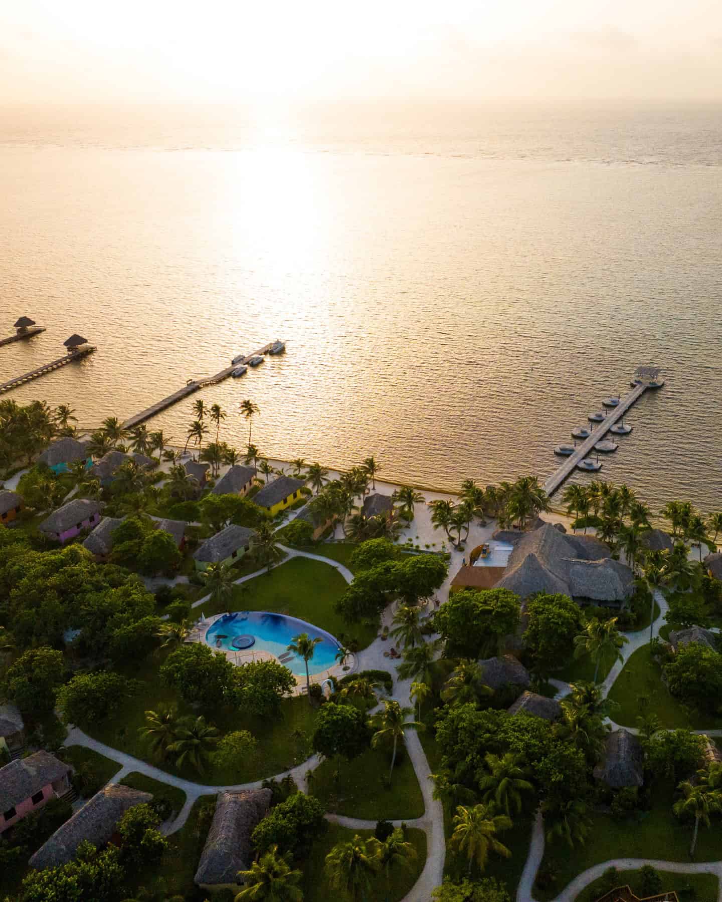 Aerial view of a coastal resort with a pool, palm trees, and docks at sunset&mdash;the perfect starting point for your Belize reef and ruins trip.
