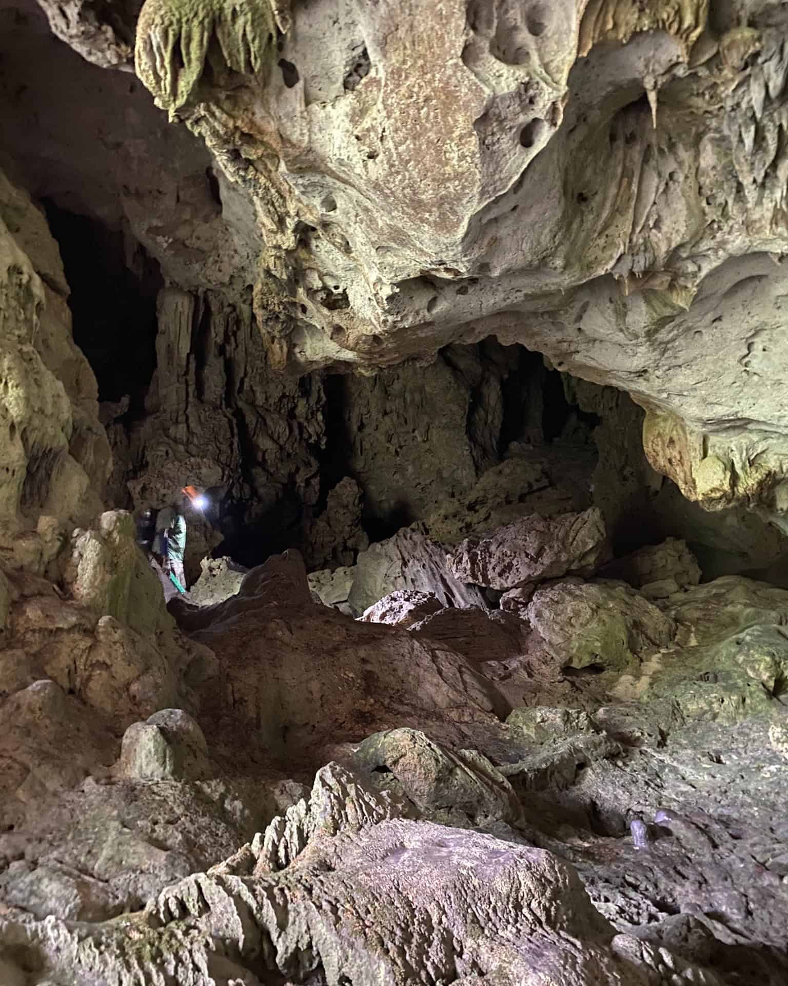 Person with a headlamp explores a rocky cave with rugged walls and uneven ground, reminiscent of discoveries on a Belize reef and ruins trip.
