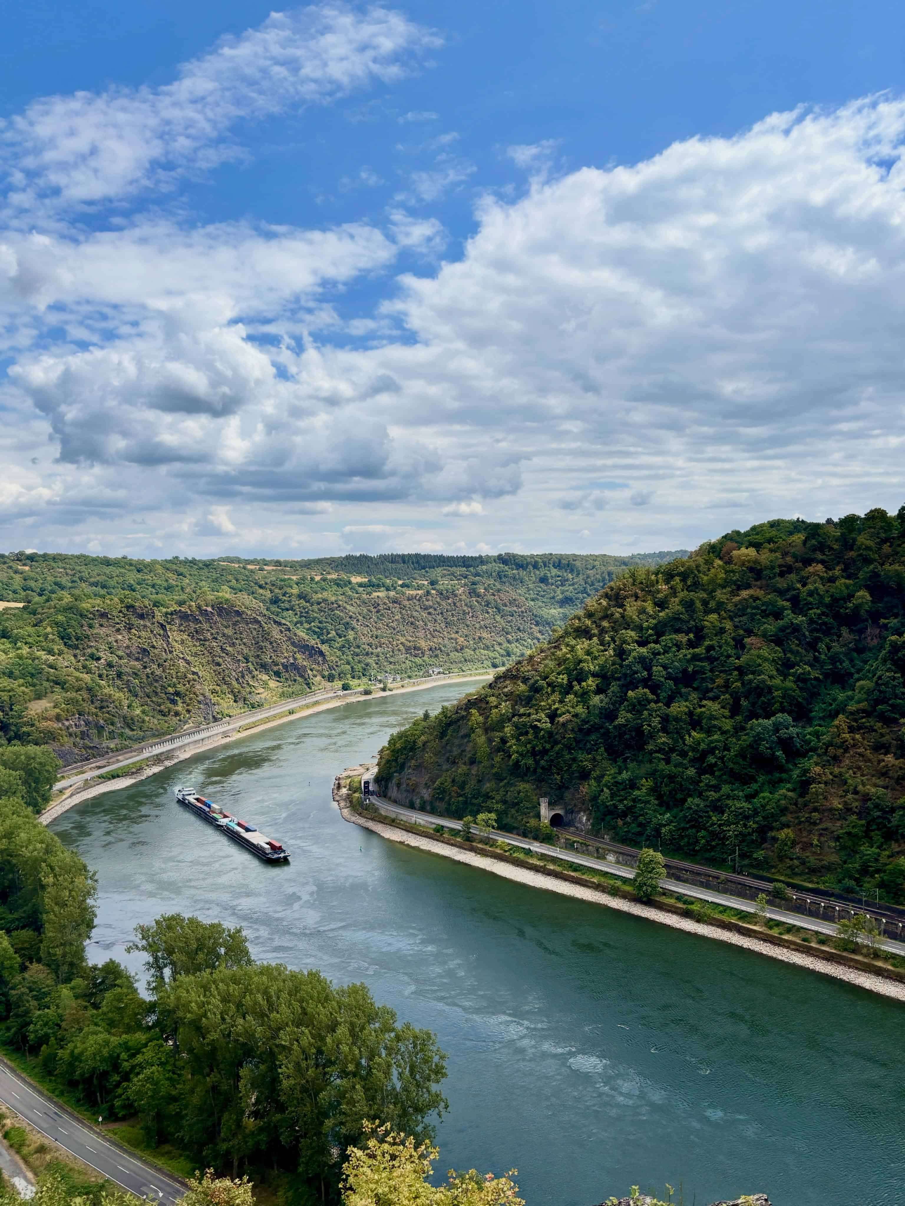 A river curves between green hills under a partly cloudy sky, with a boat traveling on the water&mdash;setting the perfect scene for a memorable Solar Eclipse Cruise.
