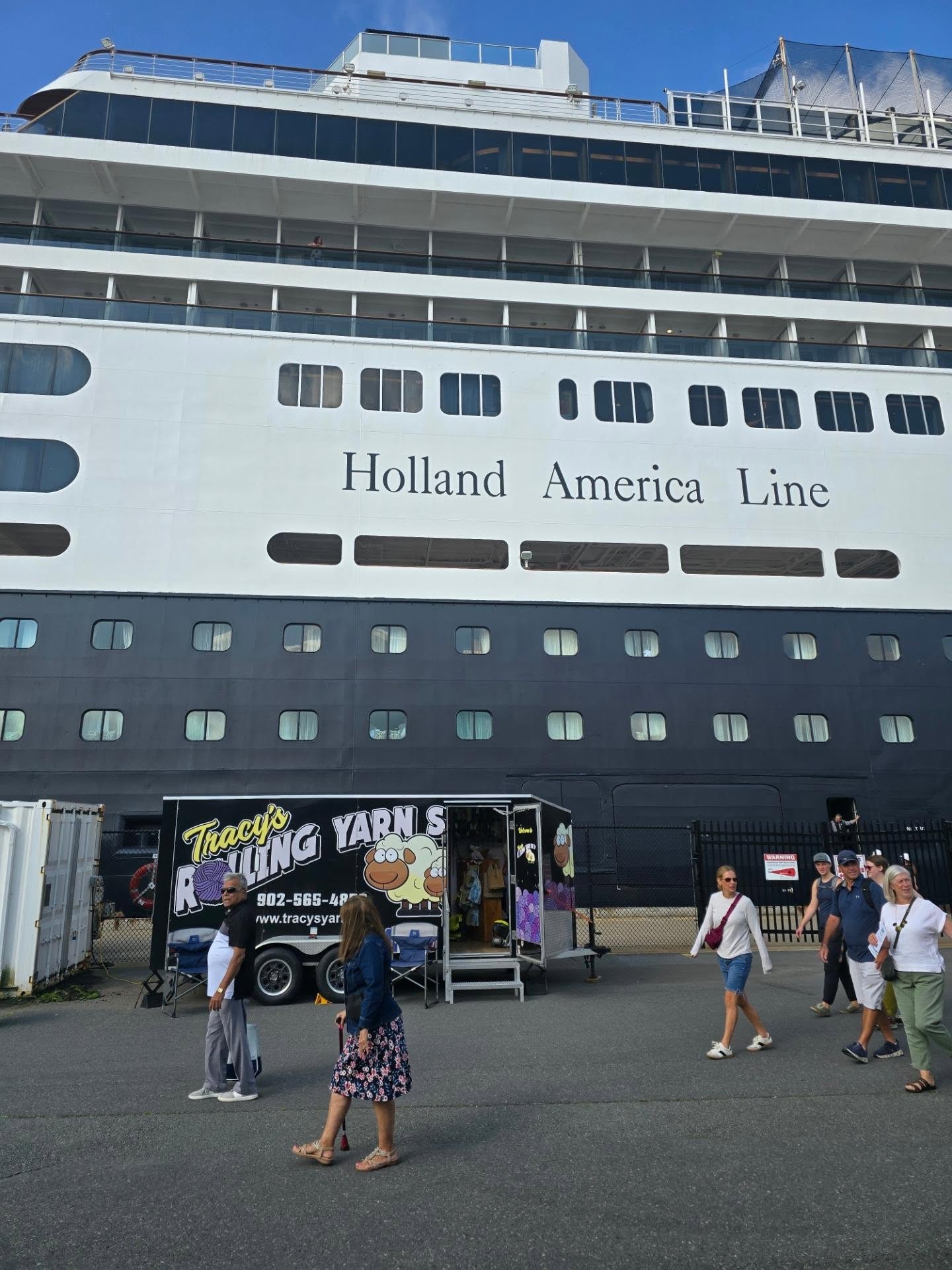 People walk by a large cruise ship&mdash;including the Solar Eclipse Cruise&mdash;and a Tracy&rsquo;s Rolling Yarns food truck in a port area under blue sky.