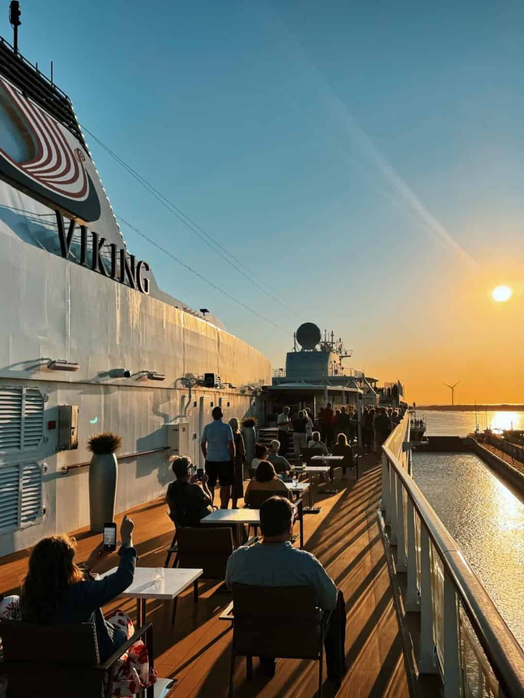 People relax on a Solar Eclipse Cruise ship deck at sunset, with the sun low over calm water and clear skies.