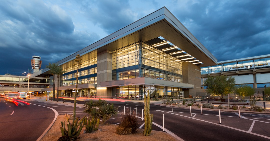 Modern airport terminal with large glass windows, desert landscaping, and cloudy evening sky, featuring a range of convenient airport amenities for travelers.