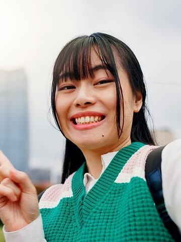 Smiling woman taking a selfie and pointing at Tokyo Tower with city buildings in the background.