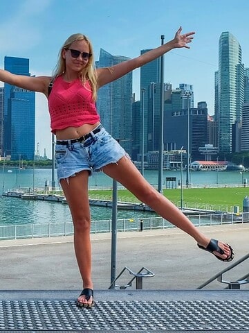 Two people pose playfully near water with city skyscrapers and modern buildings in the background.