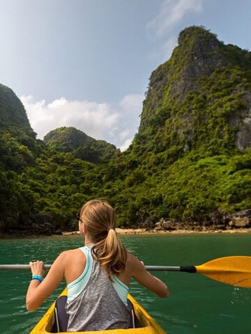 Person kayaking on turquoise water toward lush, green mountains under a partly cloudy sky—an ideal escape for those seeking countries for tourists with breathtaking natural beauty.