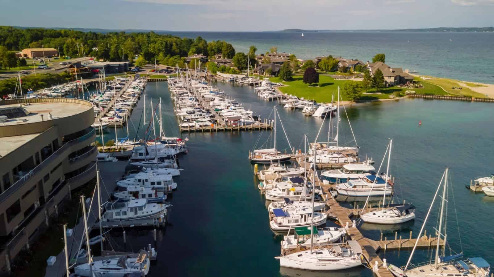 A marina with many docked boats, surrounded by green trees and buildings, next to a blue lake.